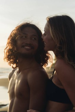 Aşık bir kadın erkeğinin arkasında durur ve usulca kulağına okyanusa karşı fısıldar. Uluslararası çift