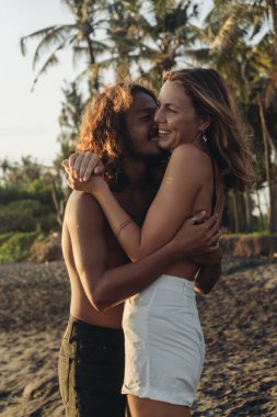 Birbirine aşık çift kumsalda gülüp, sarılır palmiye ağaçlarının arka planına.