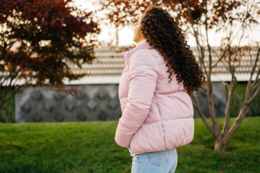 Sıradan giyinmiş bir kız parkta dikiliyor. Sırtı kameraya dönük. Lüks saçlarını gösteriyor..