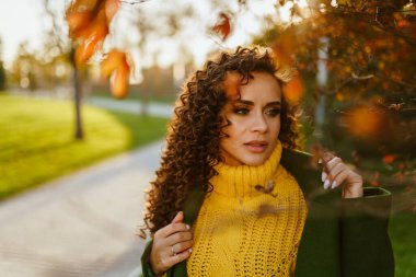 Sonbahar parkında, parlak elbiseli bir kız üzgün bir şekilde yana bakıyor ve bir el yaka palto tutuyor.