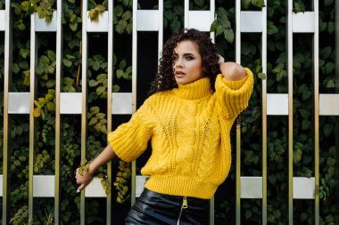 Sırtını duvara yasladı. Parlak elbiseli, şık ve güzel pozlar veren yeşil yapraklı bir kızdı.