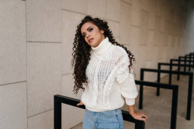 Ellerinin arkasına yaslanmış siyah saçlı kıvırcık saçlı güzel, dikkatli bir bakışla başını omzuna yaslıyor.