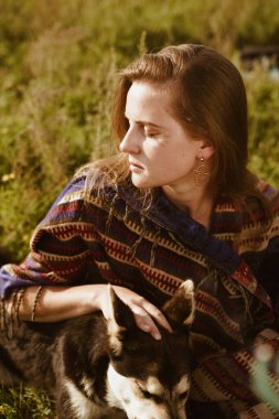 Yakın plan. Doğal güzelliği olan güzel bir kızın profili çimenlerin arasında oturmuş bir köpekle sarılıyor.