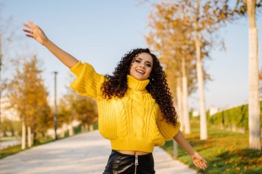 Büyük örgü ören parlak sarı bir süveter giyen neşeli kız kollarını yana doğru açarak pistteki parkta gülümsedi.