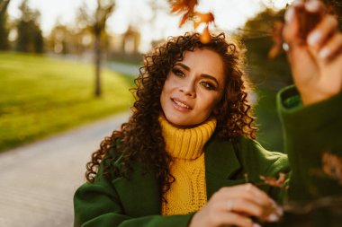 Parktaki sonbahar kıyafetleri içindeki güzel bir kadının gözlerinde hafif bir gülümseme ve ilgiyle yan yana duran baş.