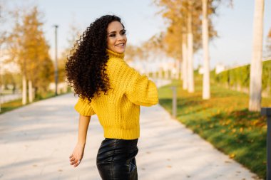 Sonbahar parkında dans eden siyah saçlı, ince kıvırcık kız.