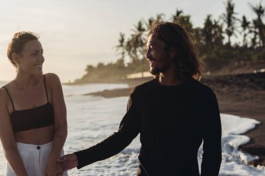 Gülümseyen bir adam, palmiye ve kumdan oluşan bir okyanusa karşılık olarak bir kadının gülümsemesini alır.