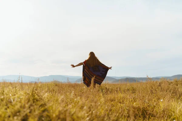 En la hierba amarilla de la estepa hacia las colinas corre una niña en una capa hasta el dedo del pie — Foto de Stock