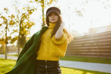 Parkta sarı bir süveter giymiş, uzun saçlarını düzelten yeşil bir ceket giymişti.