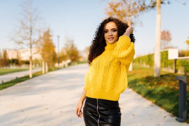 Pistte ince, kavurucu bir esmer, uzun kıvırcık saçlı ve ellerini düzelten bir tebessüm duruyor.