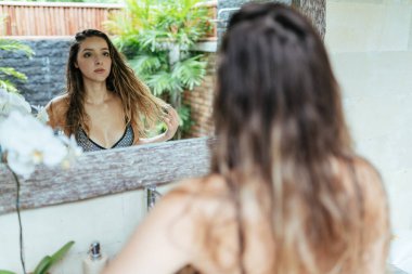 Aynaya bakınca, mayo giymiş uzun saçlı bir kız aynada kendine bakıyor.