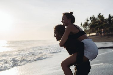 A man on the beach put a woman on his butt and they laughed at the ocean waters