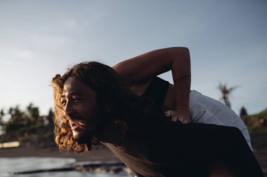 Bir adam kumsalda bir kadını gökyüzüne ve kuma karşı taşıyor. yakın plan