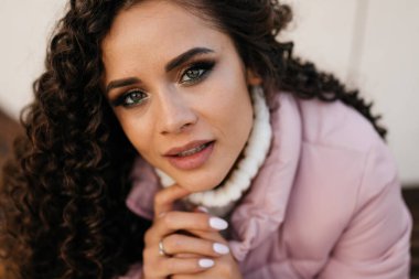 Yakın plan. Uzun kıvırcık saçlı, güzel bir esmerin yeşil gözleri süveterin yakasına dokunuyor.