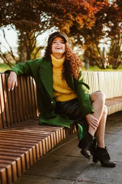 Parkta oturan bir kız ayağını bacağına attı ve kafasını havaya kaldırarak neşe içinde güldü.