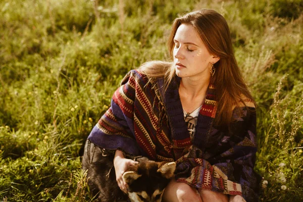 Sobre la hierba se sienta una chica con los ojos cubiertos con una bufanda y acaricia al perro — Foto de Stock