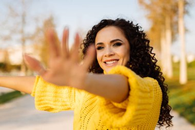 Yakın plan. Güzel bir gülüşü ve siyah kıvırcık saçları olan kız ellerini perdeye çekiyor.