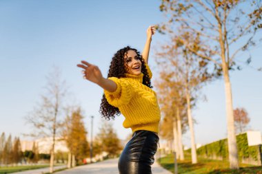 Sonbaharda parkta rahat bir şekilde esnemiş bir kız. Parlak sarı bir kazak giymişti.