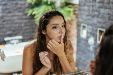 Dikkatlice aynaya bakıyor ve banyoda güzel bir kızın dudaklarına dokunuyor.