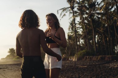 Karanlık kum ve palmiye ağaçlarının arka planında birbirini seven bir çift duruyor ve gülümsüyor.