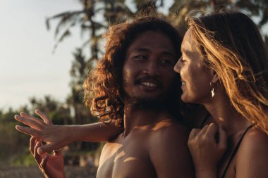 Çıplak omuzlu bir kadın ve bir erkek, palmiye ağacında birbirlerine sevgiyle bakıyorlar.