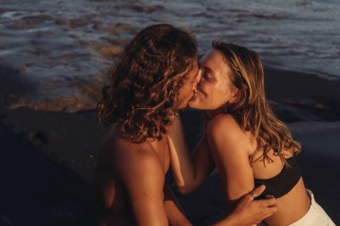 Aşık bir adam ve kadın okyanus arka planında öpüşürler kayaların üzerinde otururlar