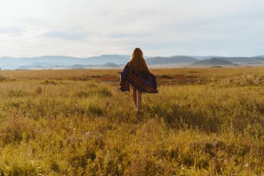 Renkli bir pelerinle çıplak ayakla kaçıyor bozkırdaki otların üzerinde dalgalanan uzun saçlarıyla tepelere doğru