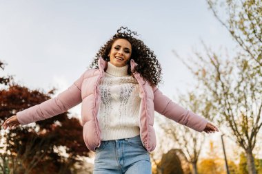 Rüzgara doğru esiyor. Kıvırcık kıvırcık saçlı, siyah saçlı, ceketli ve kot pantolonlu.
