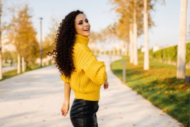 Parktaki pistte parlak sarı bir kazak içinde durmuş gülüyor güzel esmer