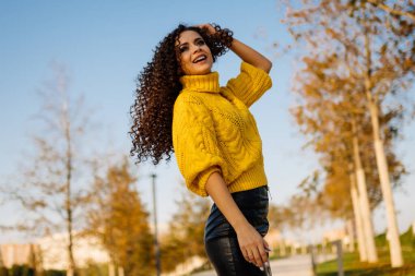 Sonbahar parkında büyüleyici bir gülümseme ile kıvırcık esmer duruyor.