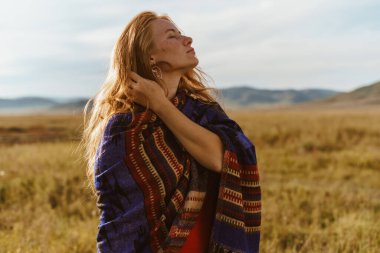 Yüzünü tarlaya koyan kız çizgili bir pelerine bürünmüş ve gözlerini kapamış bir tepenin arkasında saçına dokunuyor.