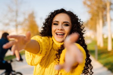 Kız parkta koşar kollarını uzatır ve neşeyle gülümser.