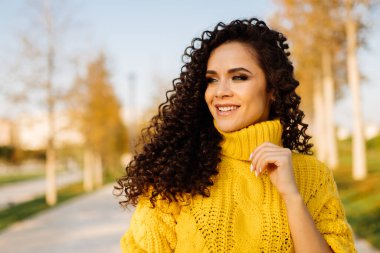 Ağaçlardaki sarı sonbahar yaprakları güzel bir gülüşü olan sarı kıvırcık esmer süveterle uyumlu.