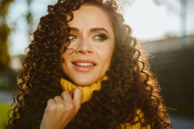 Omuzlarının üzerinden gülümsüyor yeşil gözlerle uzaklara bakıyor. Kıvırcık esmer yakın plan.