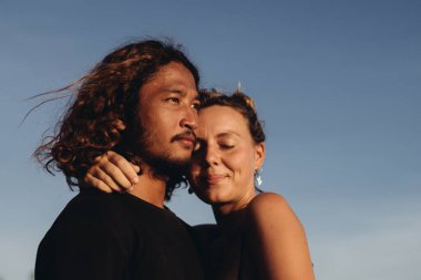 Mavi gökyüzüne karşı, Asyalı görünümlü bir adamın yüzü ve gözleri kapalı bir kadının sarılmış yüzü.