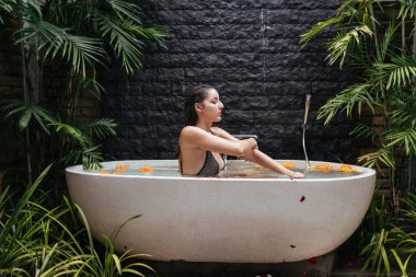 Açık havada suyla ve çiçeklerle dolu bir küvette güzel bir kız kaplıca ameliyatı oluyor.