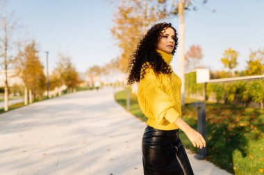 Sonbaharda park yoluna parlak sarı kazaklı bir kız gelir siyah bukleleri omuzlarına yayılır.