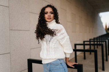 Kız ellerini arkasına yasladı ve beyaz bir kazak ve kot pantolon içinde tünelde durdu. Koyu renk saçları omuzlarının üzerine yayıldı.