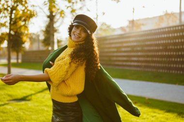 Bright beautiful girl in a bright yellow sweater whirling in the park throwing on one shoulder coat