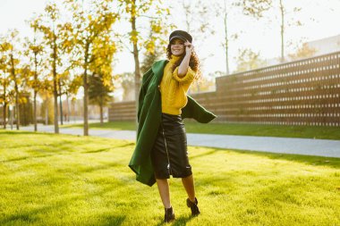 Parktaki yeşil çimenlerde yürür. Güzel bir kız şapkasını kafasına geçirir ve ceketini bir omzunun üzerinden atar.