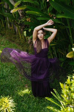 Arka planda muz palmiyelerinin arasında kızların elinin arkasında katlanmış uzun bir elbise duruyor.