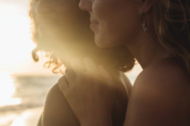 Bir erkeğin ve bir kadının okyanusa karşı gülümseyen yüzlerinin alt kısımlarına yakın çekim.