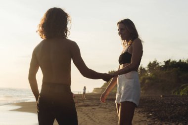 Okyanusta kumların üzerinde bir çift aşk kuşunun elini tutan bir çift kadın ve erkeğin.