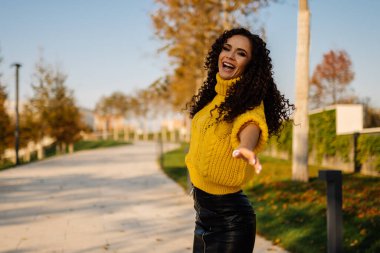 Parktaki pistte açık ağızlı, parlak bir kazak ve deri etekli kıvırcık esmer bir eli ileri koyarak şarkı söylüyor.