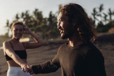 Öndeki adam kadının elini tutuyor ve onu palmiye ağaçlarına doğru çekiyor.