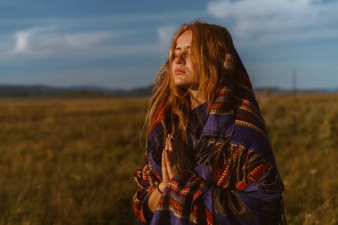 Dua ederek katlanmış eller ve başını ve omuzlarını pelerinle kapatmış sarı otçu kızın tarlasında duruyor.