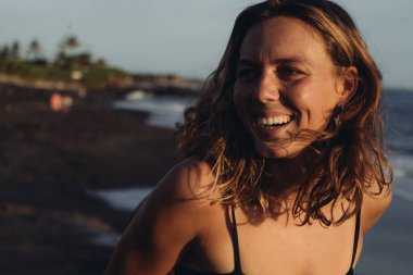 Okyanusun ve sahil kumunun arka planında neşeli bir gülümsemesi olan güzel bir kız. yakın plan