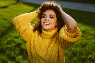 Kıvırcık esmer tüylü, kalın saçlı ve yeşil çimenlerin arkasında kurnazca gülümseyen.