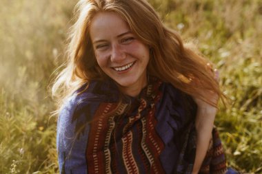 Çayırda güzel bir kız oturuyor. Buğday rengi saçlı, yüzünde çiller ve neşeli beyaz dişli bir gülüşü olan.