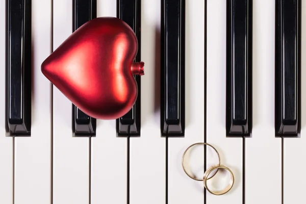 Teclado piano, coração vermelho e anéis de casamento — Fotografia de Stock